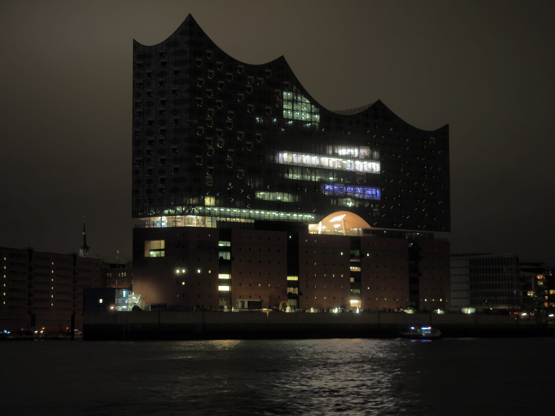 The Elbphilharmonie in Hamburg lit at night, seen across the water from the harbor side.