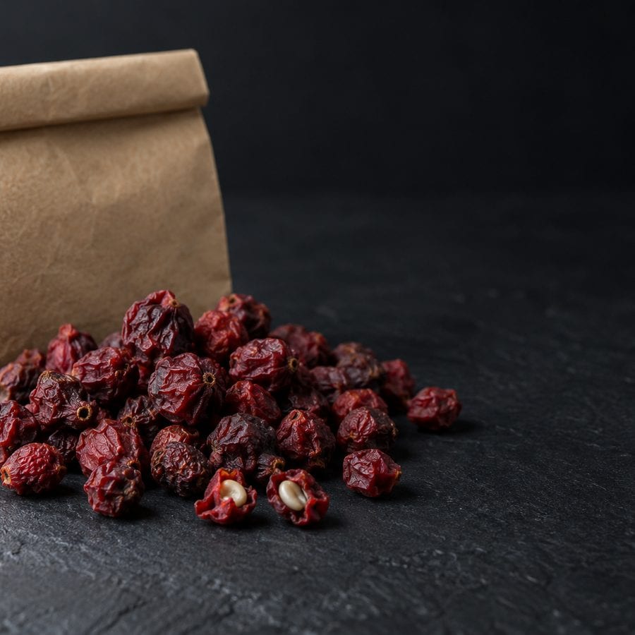 Dried deep red omija berries spilling from a brown paper bag onto dark slate.